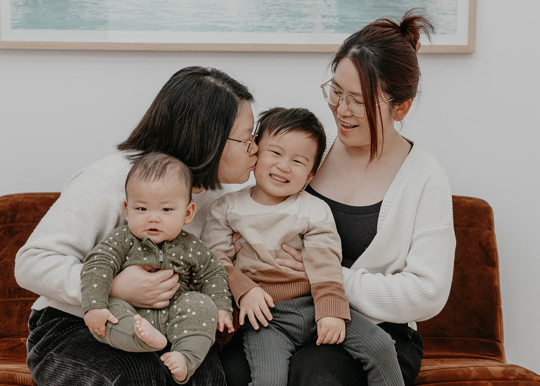 Two women sitting on a couch with two children, one of whom is being kissed on the cheek.