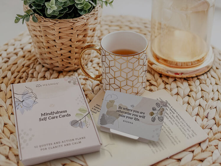 Mindfulness self-care cards, tea mug, and calming desk accessories arranged on a woven table mat