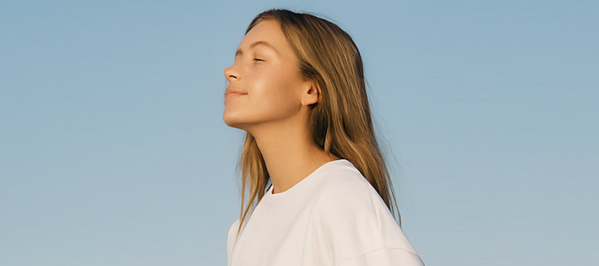 Woman with eyes closed against a clear blue sky