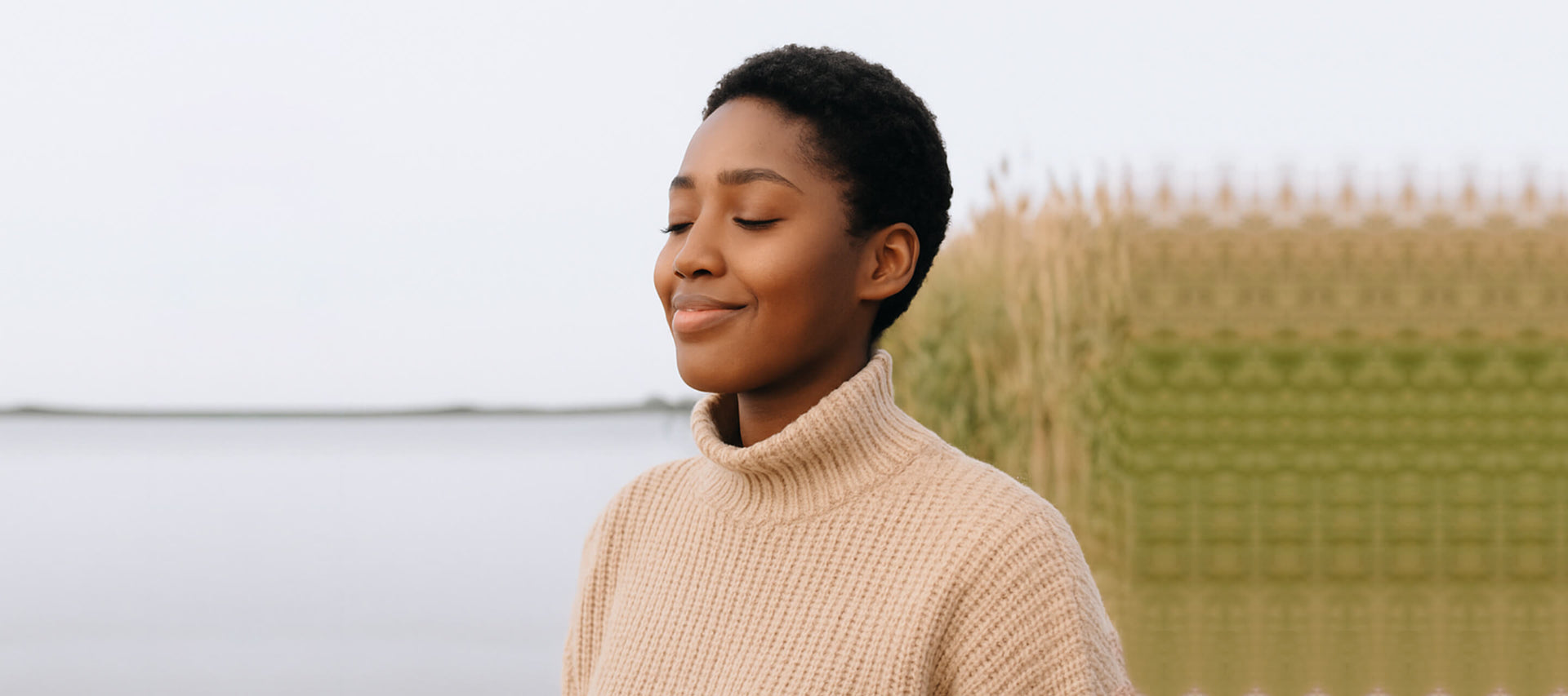 Woman wearing a beige sweater standing outdoors with a blurred natural background