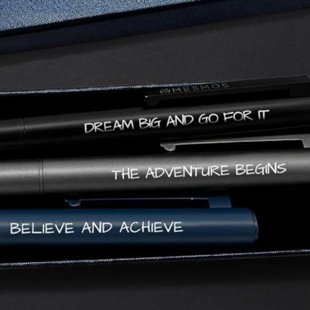 Three pens in a box with 'MESMOS' branding on a desk with a keyboard and notebook.